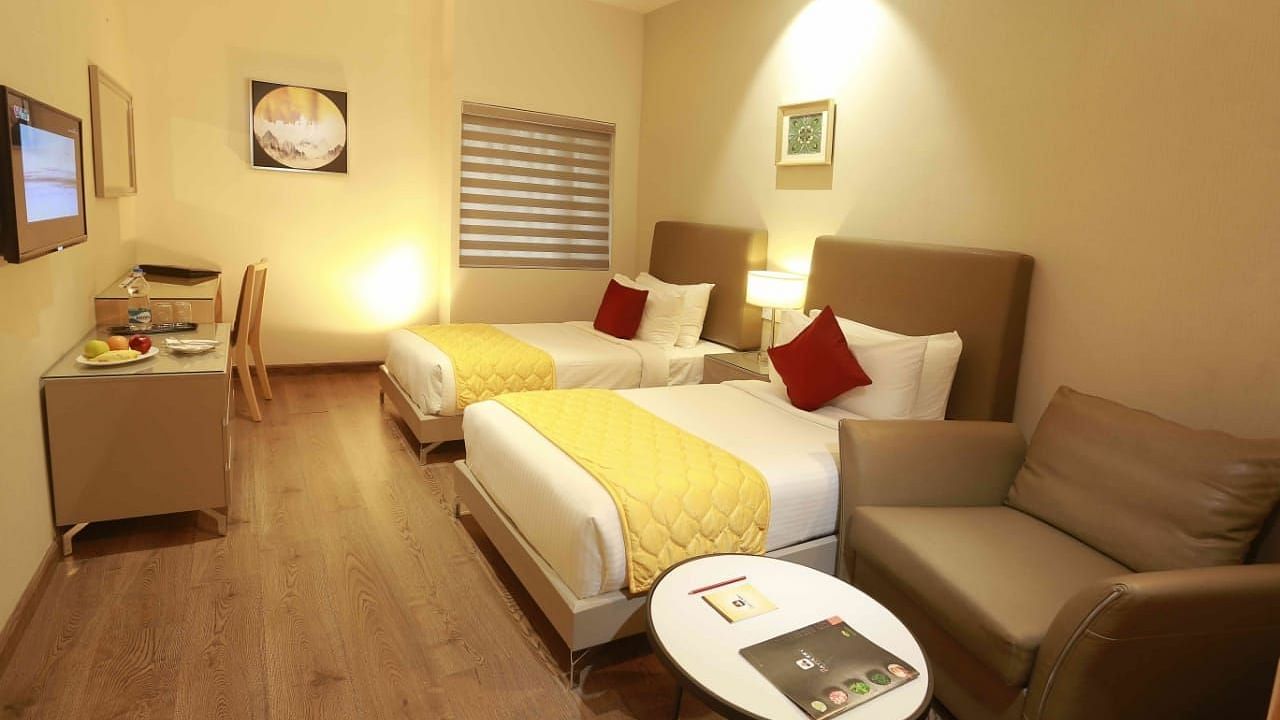 Premium Twin Room at Mayberry Tiruppur featuring twin beds, a sofa, and a small coffee table